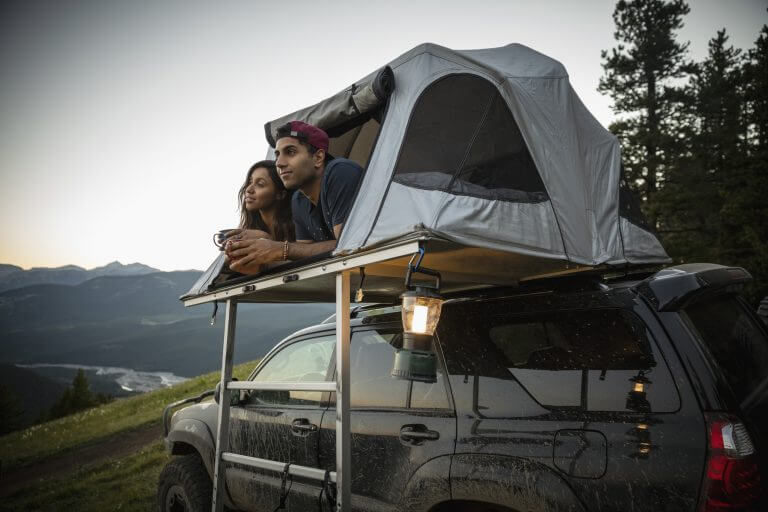 A couple camping on the top of a car financed with a credit union auto loan in Washington state.